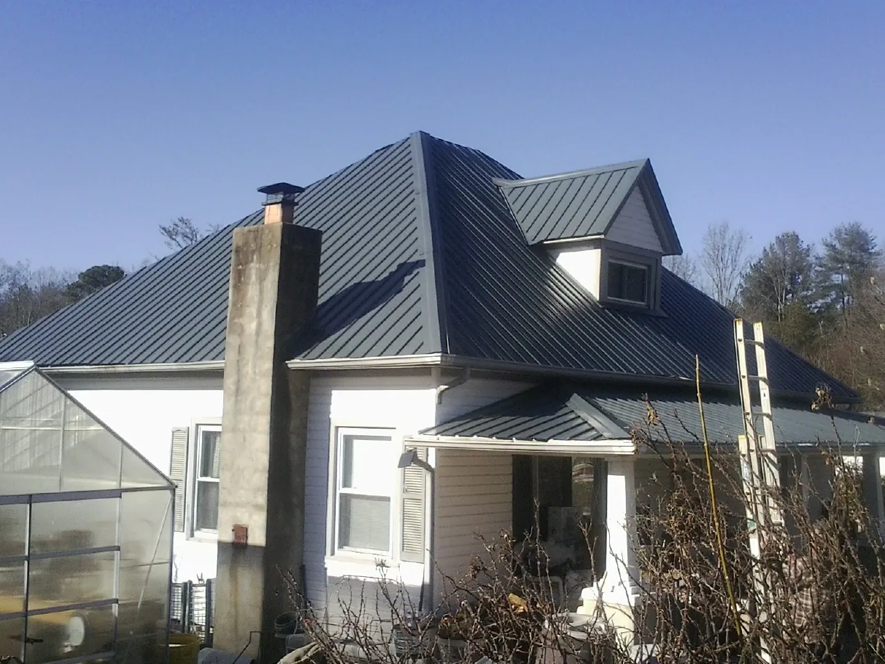 Dark blue standing seam metal roof on a white farmhouse with dormer — Slate & Tile Roof Repair by Roofing Brothers in Elbert