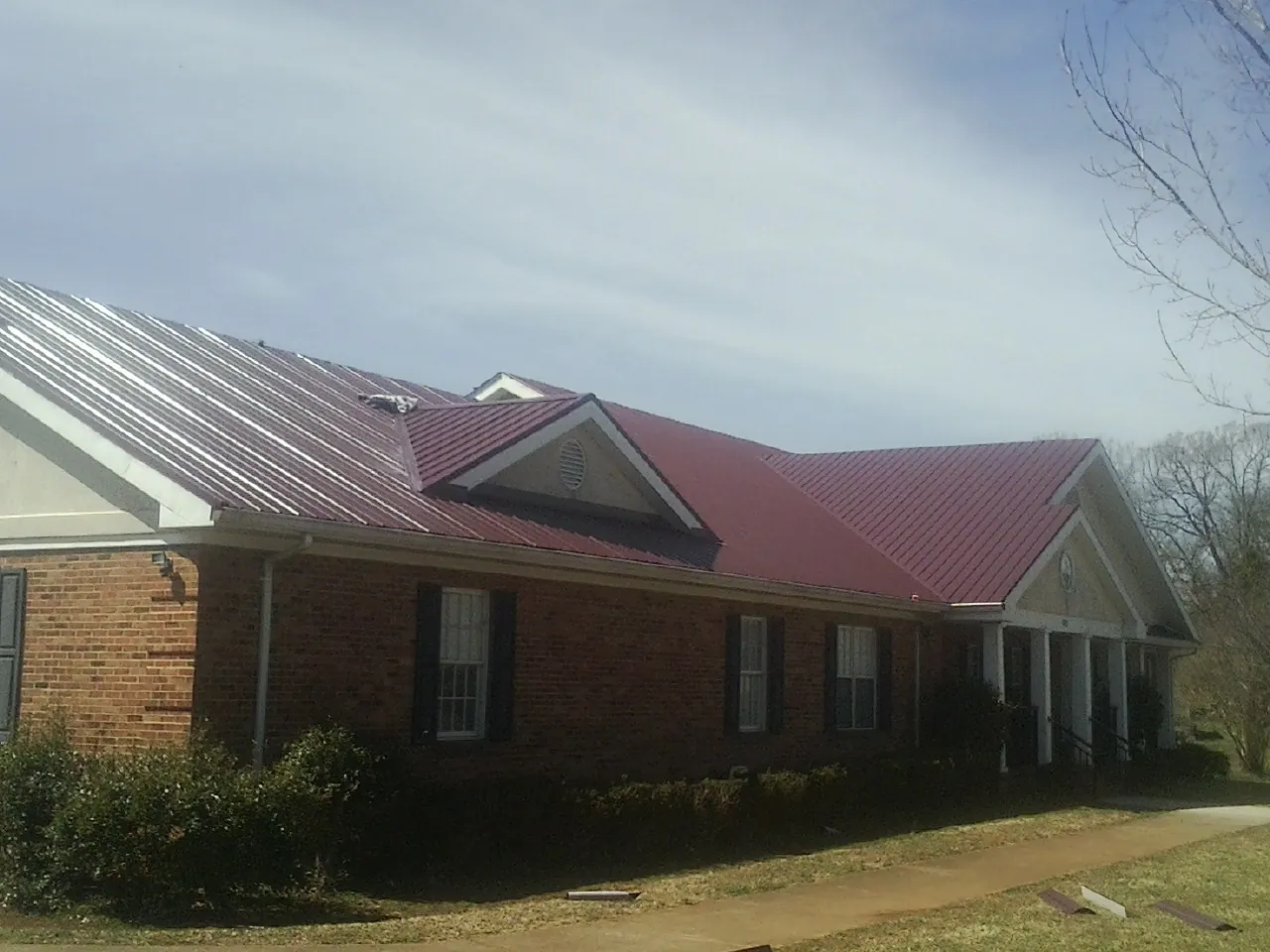 Red metal roof with gabled entries on a long brick building, from a Hail Damage Roof Repair job in Elbert