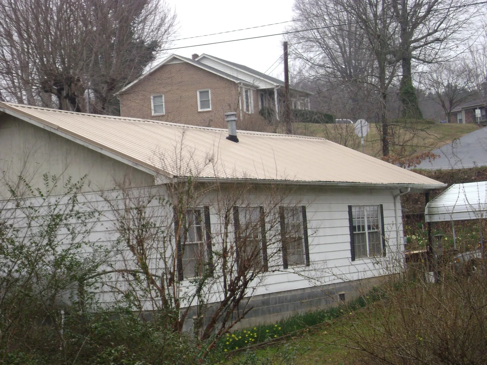 Tan metal roof on a white sided house set into a hillside — Commercial Roofing by Roofing Brothers in Elbert