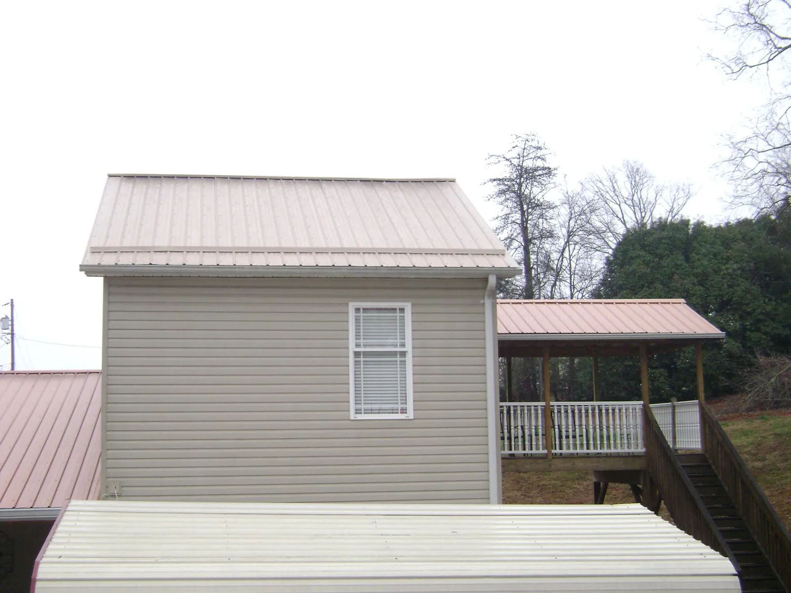 Tan metal roofs on a two story addition and attached porch, from a Roof Replacement job in Elbert